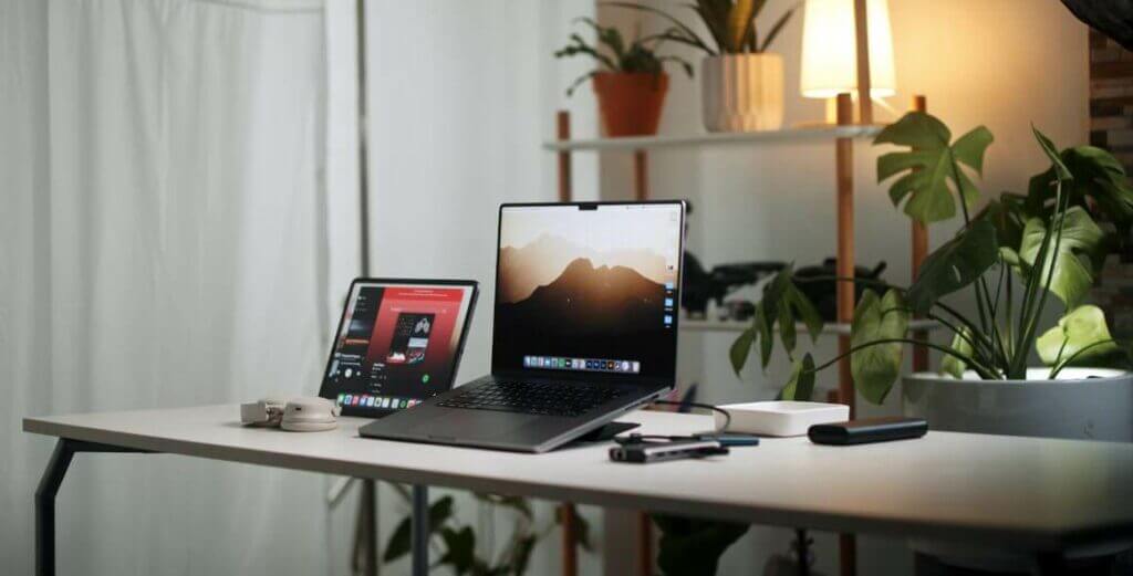 A simple desk design with two laptops, a tablet, and a plant.