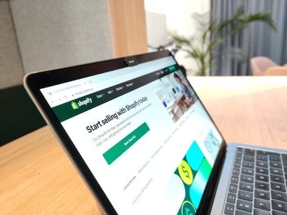 A laptop is sitting on a wooden table while the owner works on building a website using the ultimate guide for 2024.
