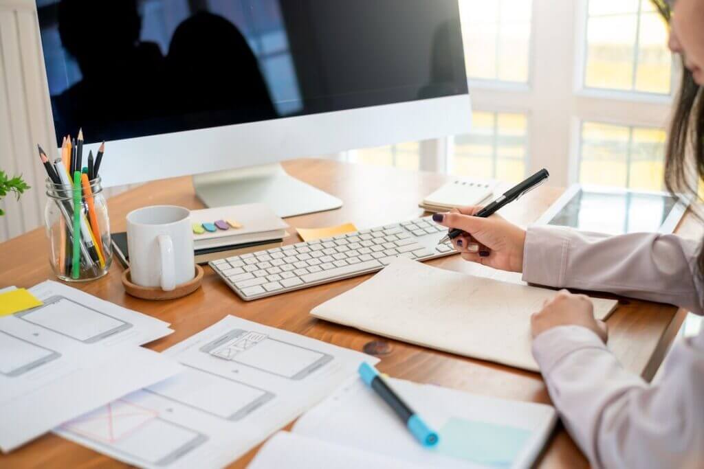 A woman is working at a desk with a notebook and a computer, focusing on website optimization and SEO keywords.